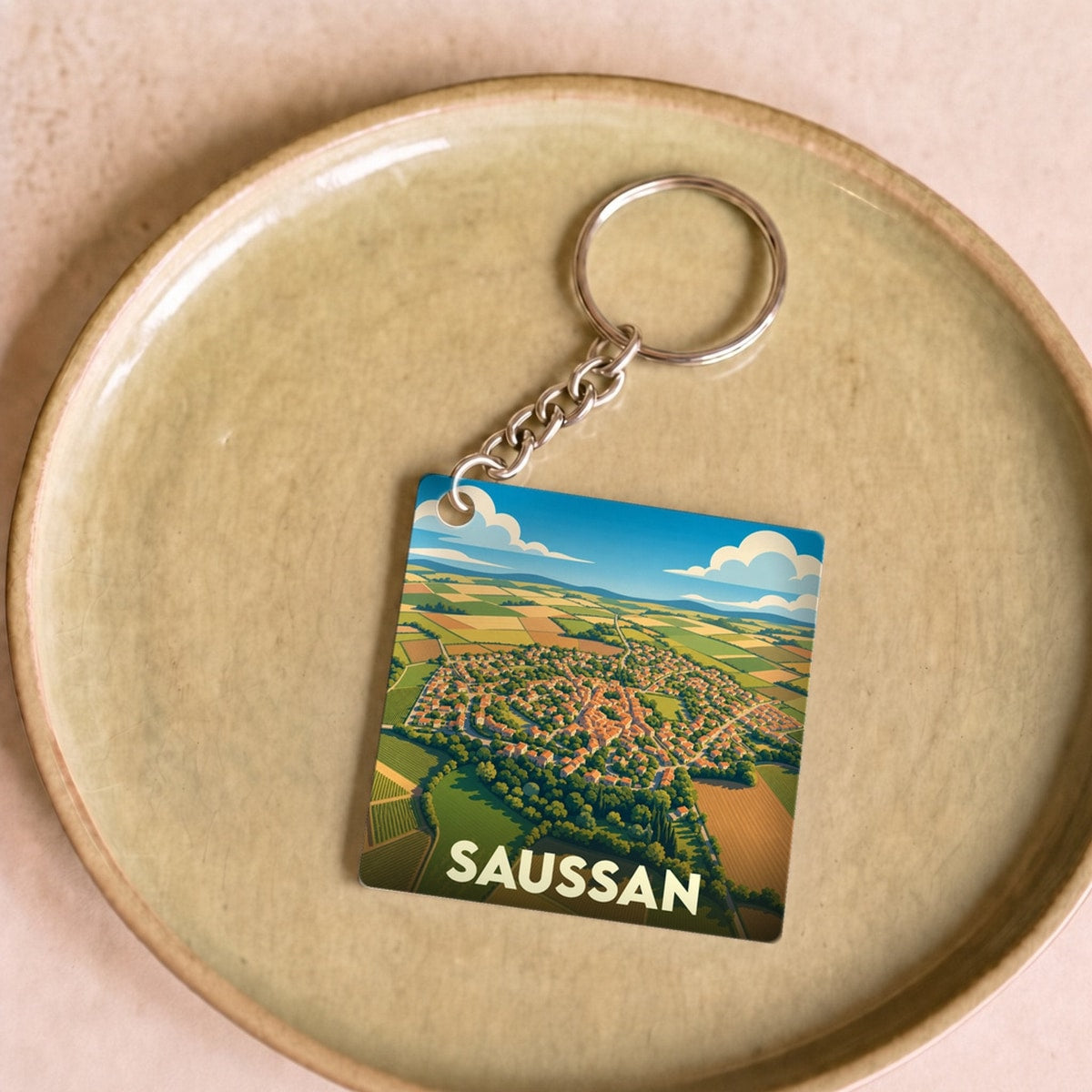 Porte-clés souvenir de la ville de Saussan avec une illustration aérienne stylisée du village et de ses champs.