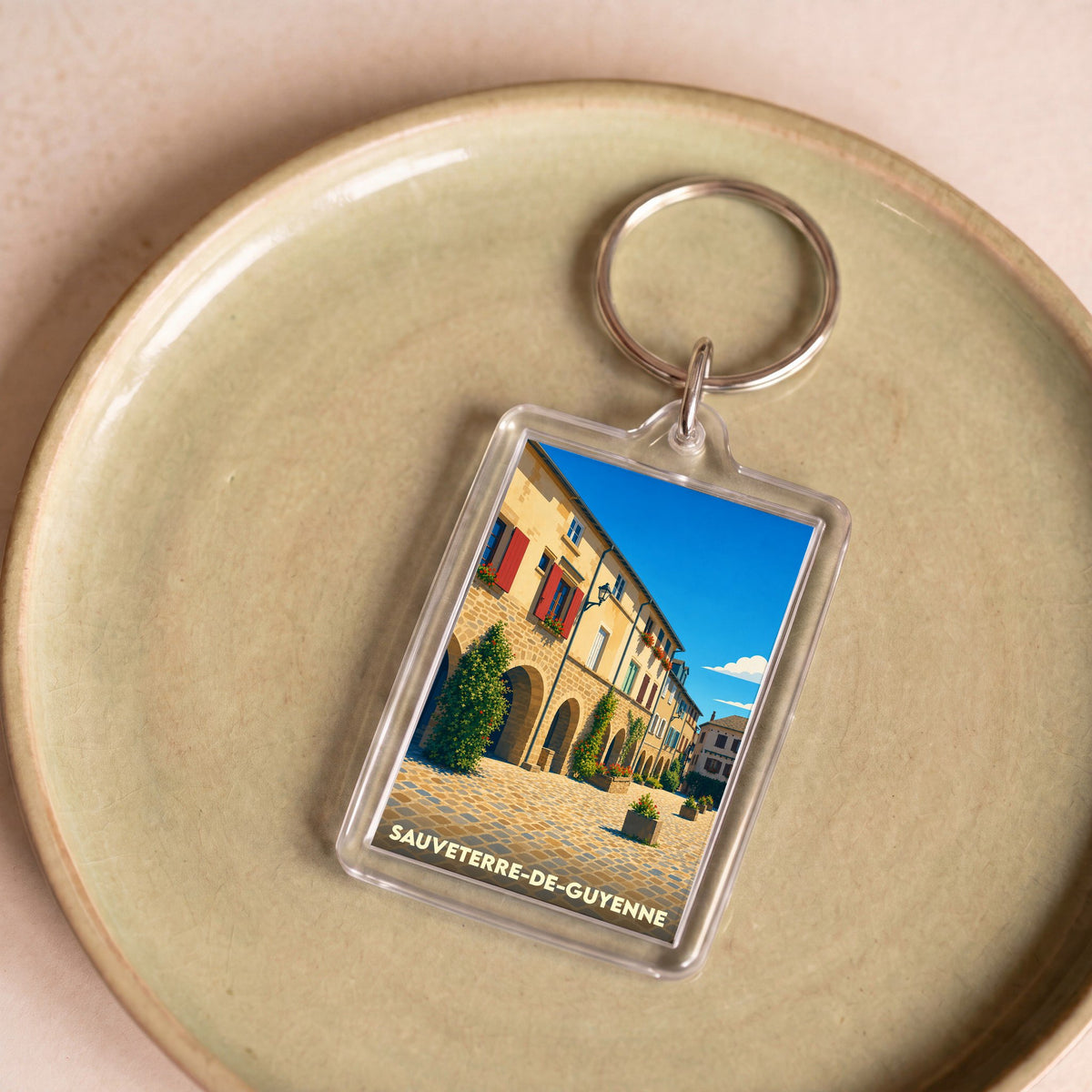 Porte-clés souvenir de la ville de Sauveterre-de-Guyenne avec une illustration stylisée d'une place historique.