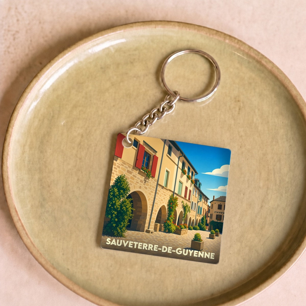 Porte-clés souvenir de la ville de Sauveterre-de-Guyenne avec une illustration stylisée d'une place historique.