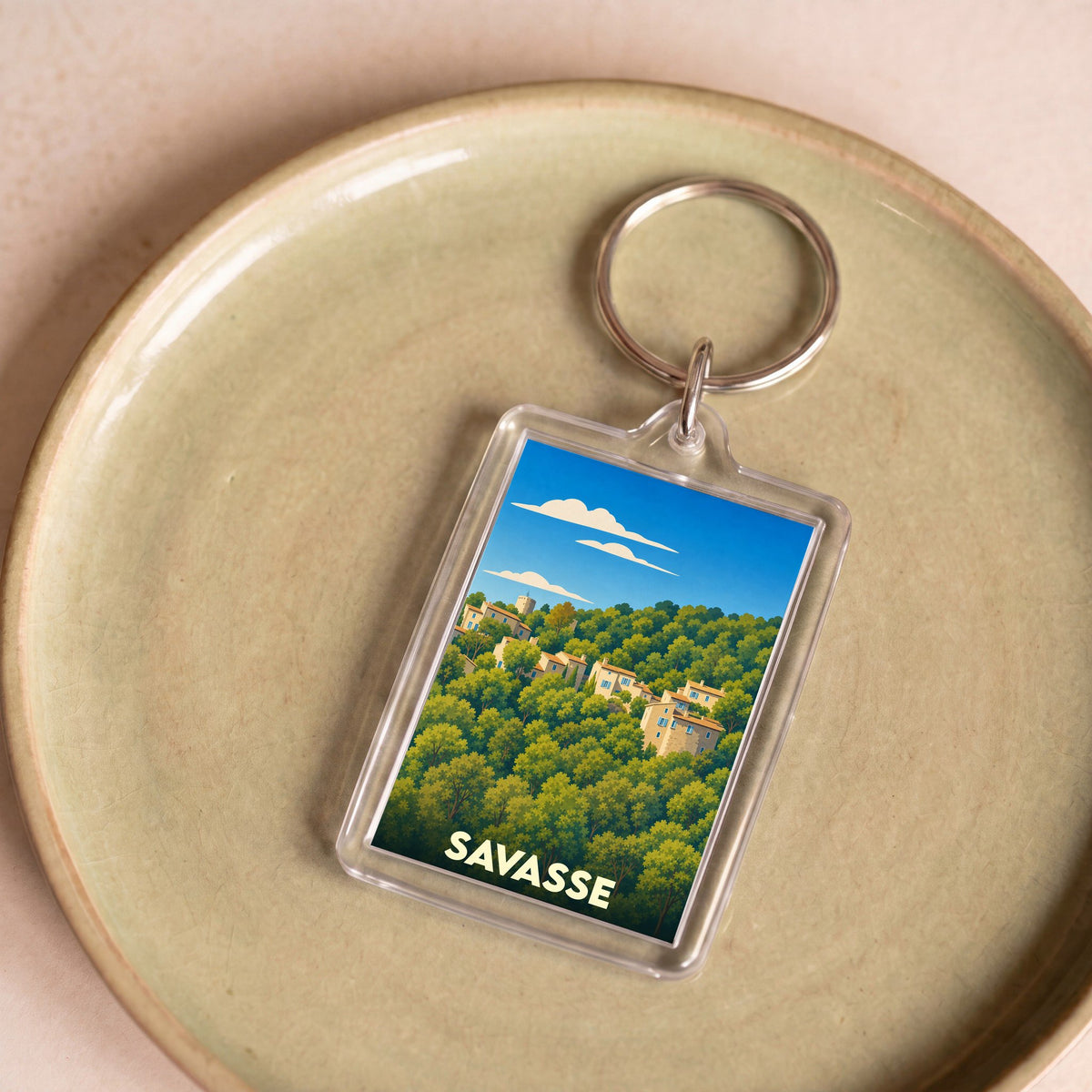 Porte-clés souvenir de la ville de Savasse avec une illustration stylisée d'un village niché dans la forêt.