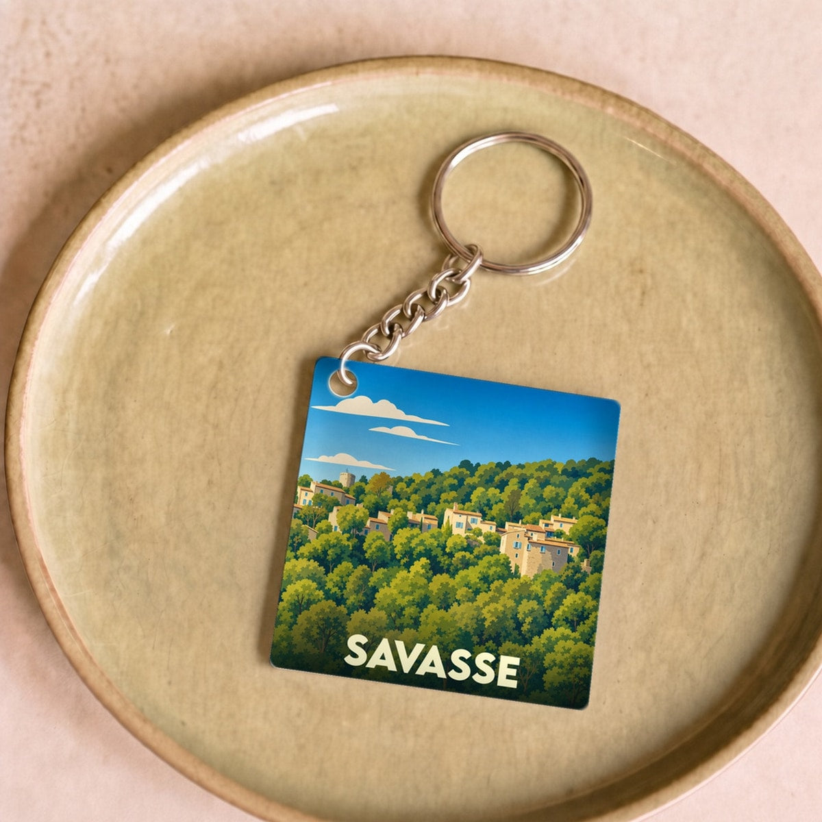 Porte-clés souvenir de la ville de Savasse avec une illustration stylisée d'un village niché dans la forêt.