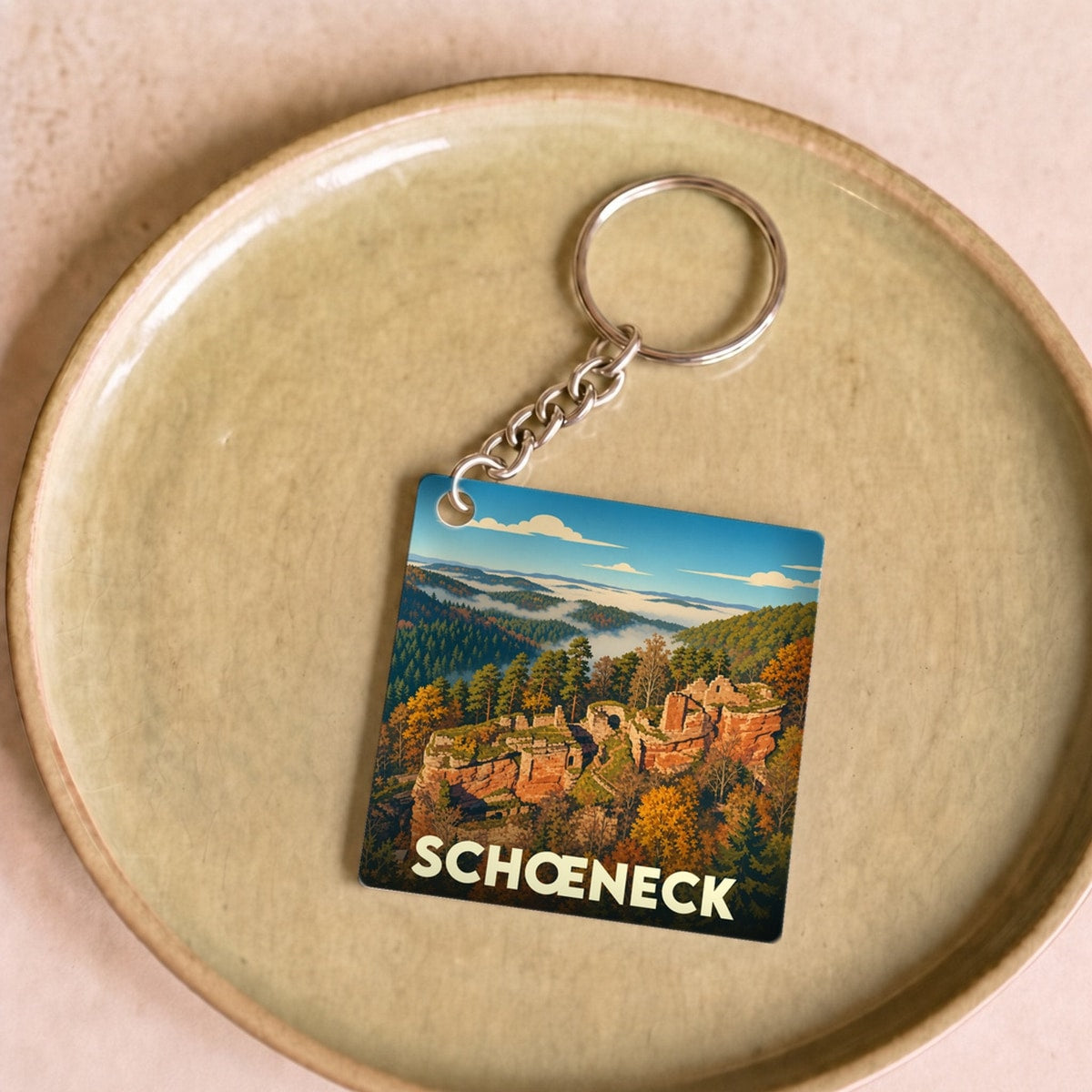 Porte-clés souvenir de la ville de Schœneck avec une illustration stylisée de son paysage forestier et rocheux.