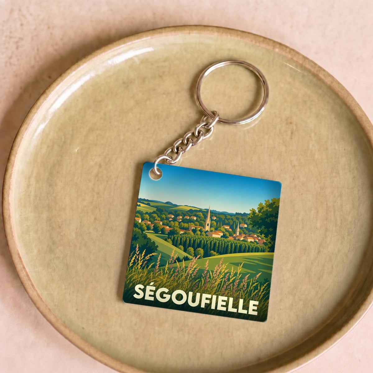 Porte-clés souvenir de la ville de Ségoufielle avec une illustration stylisée de son paysage champêtre.