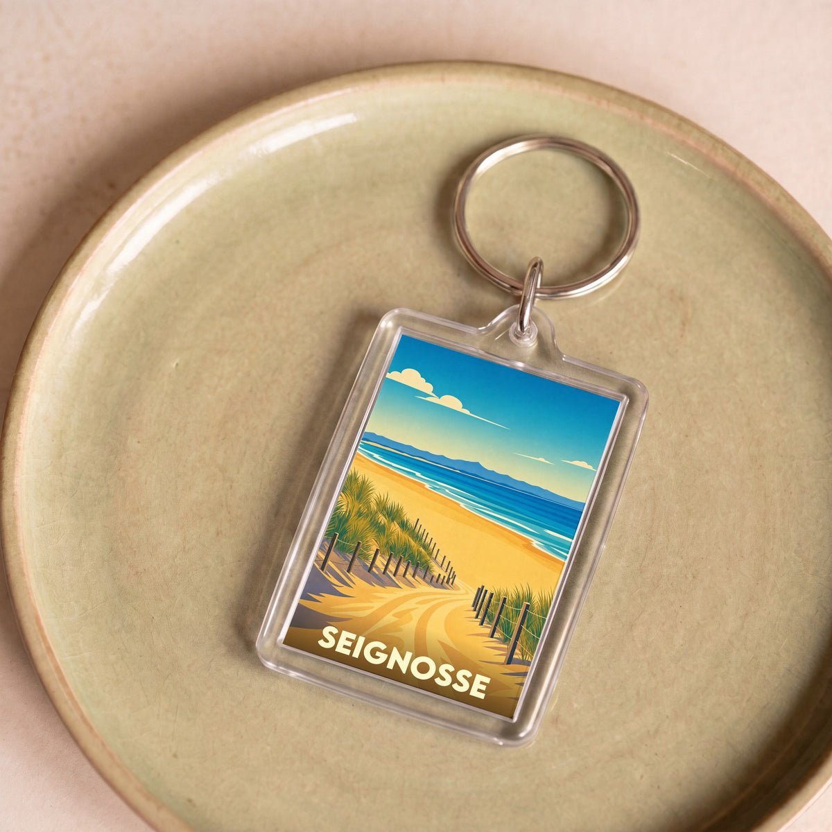 Porte-clés souvenir de la ville de Seignosse avec une illustration stylisée d'un chemin dunaire menant à l'océan.
