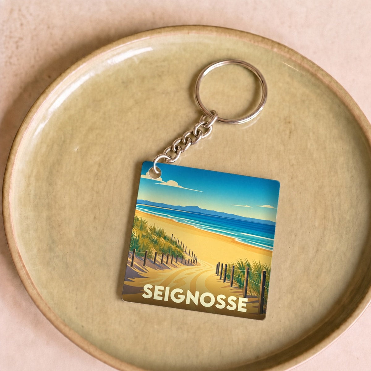Porte-clés souvenir de la ville de Seignosse avec une illustration stylisée d'un chemin dunaire menant à l'océan.