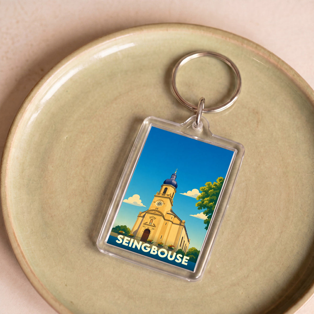 Porte-clés souvenir de la ville de Seingbouse avec une illustration stylisée d'une église sous un ciel bleu.