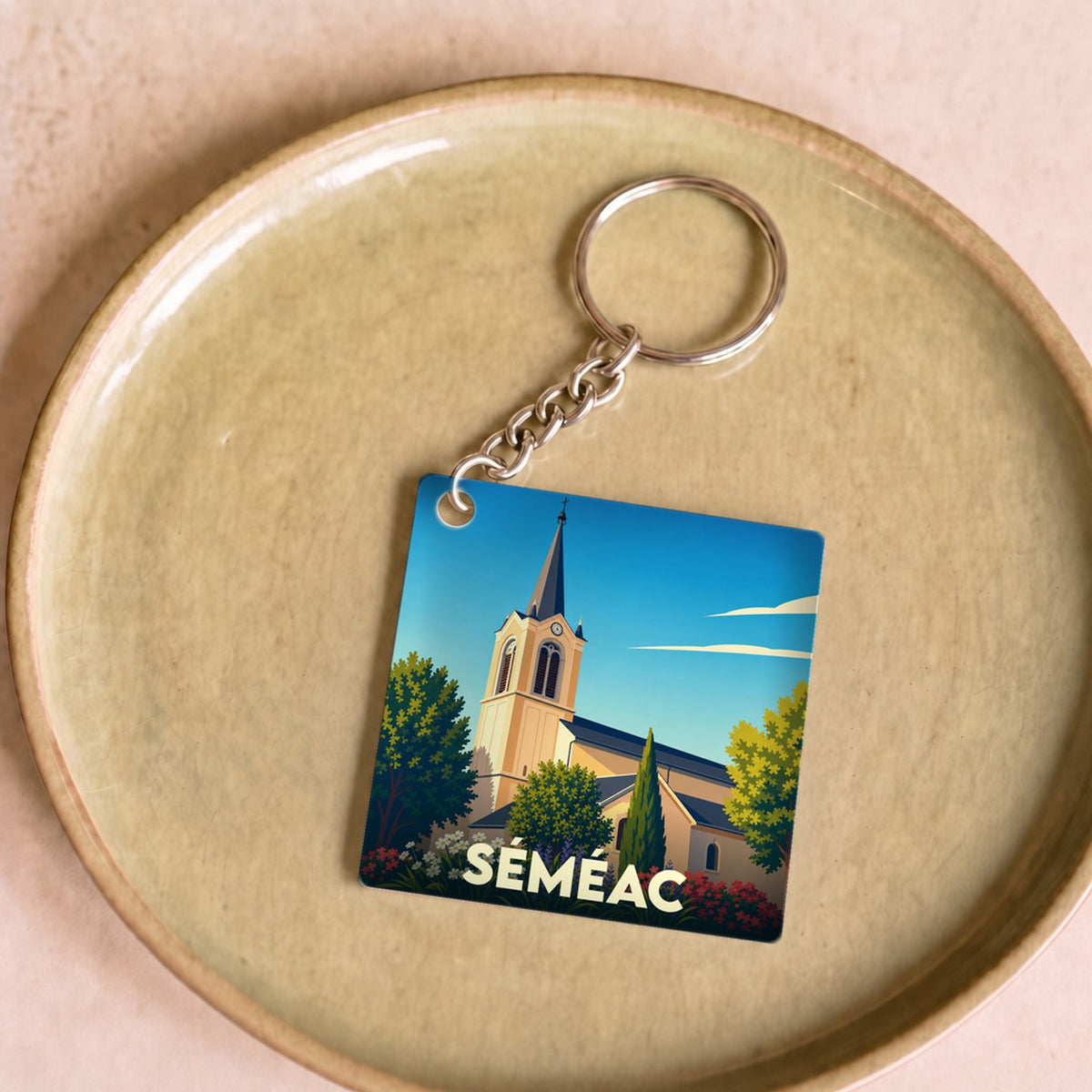 Porte-clés souvenir de la ville de Séméac avec une illustration stylisée de son église et de jardins fleuris.