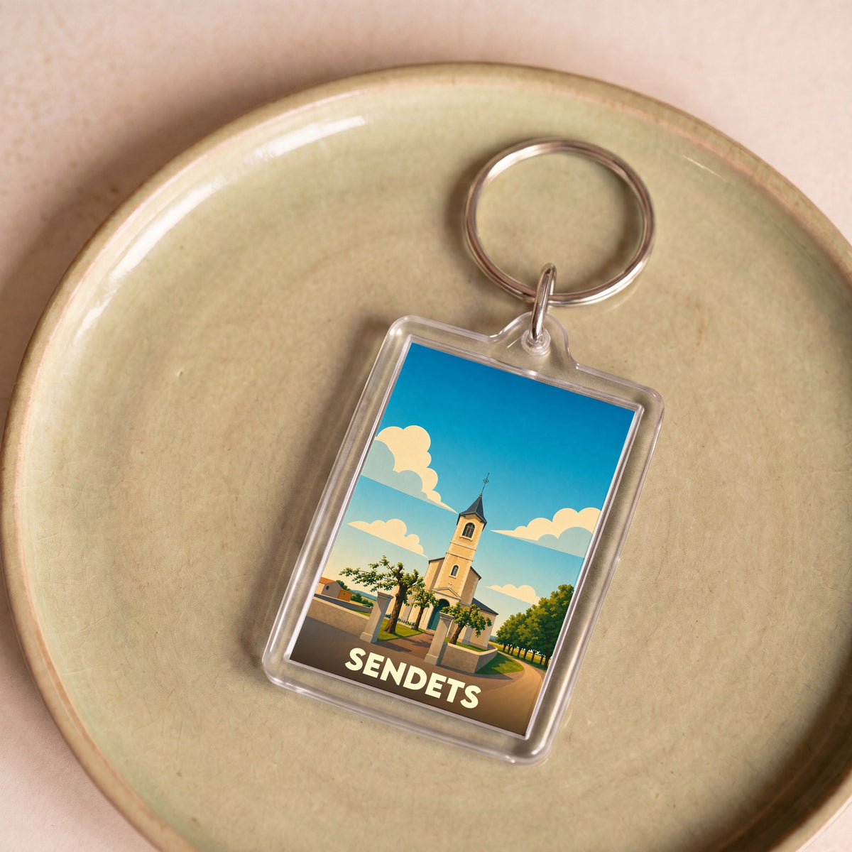 Porte-clés souvenir de la ville de Sendets avec une illustration stylisée de son église sous un ciel bleu.