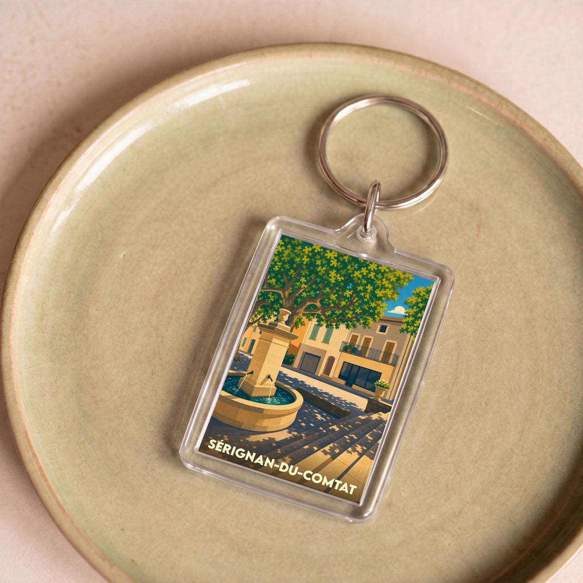 Porte-clés souvenir de la ville de Sérignan-du-Comtat avec une illustration stylisée d'une fontaine provençale.