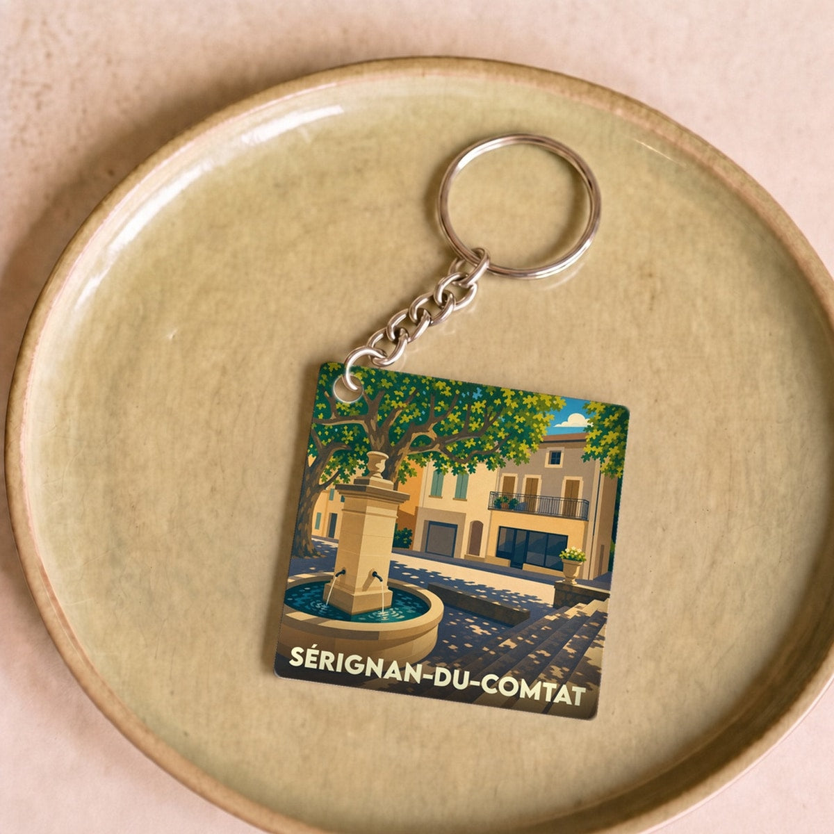 Porte-clés souvenir de la ville de Sérignan-du-Comtat avec une illustration stylisée d'une fontaine provençale.