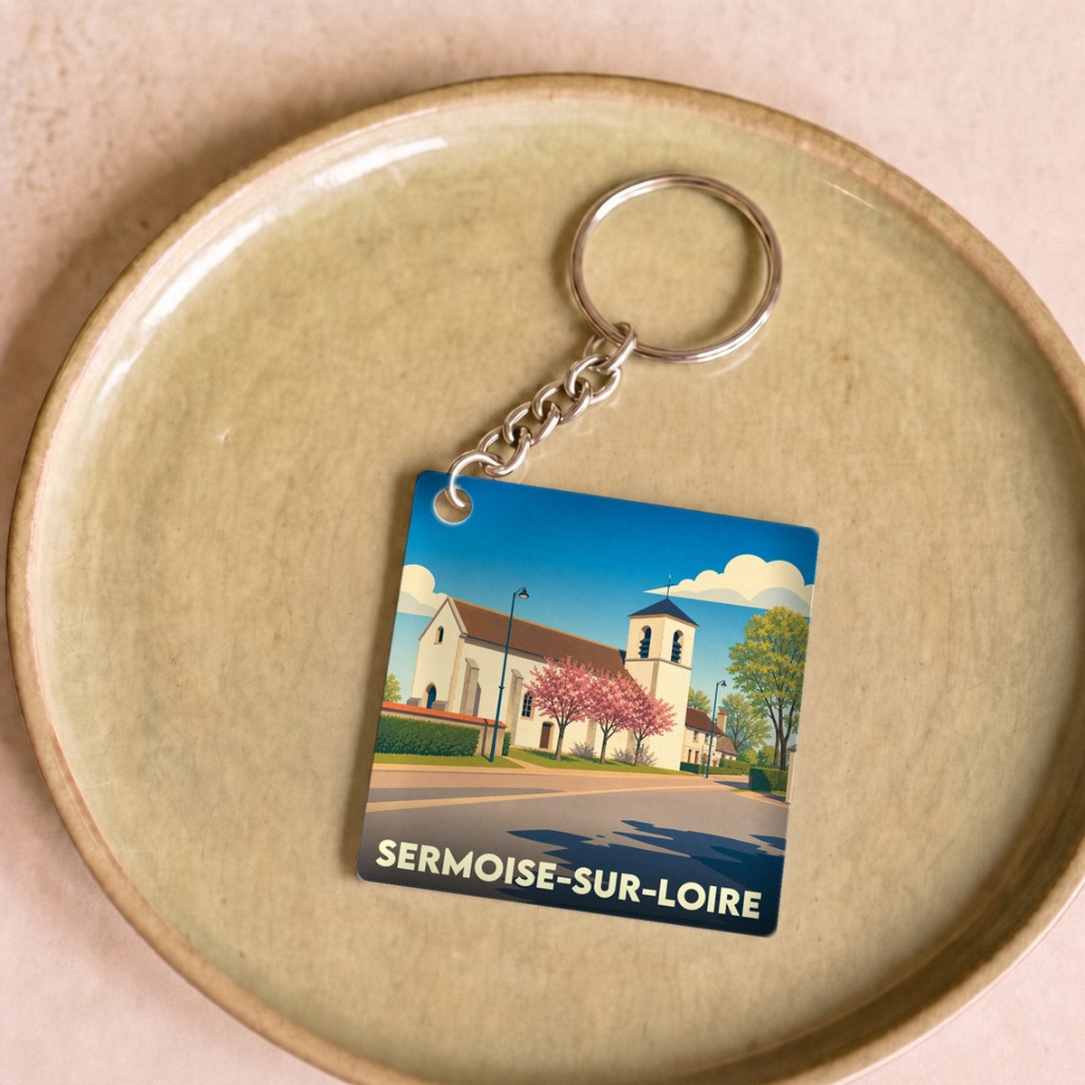 Porte-clés souvenir de Sermoise-sur-Loire avec une illustration stylisée de son église sous un ciel bleu.