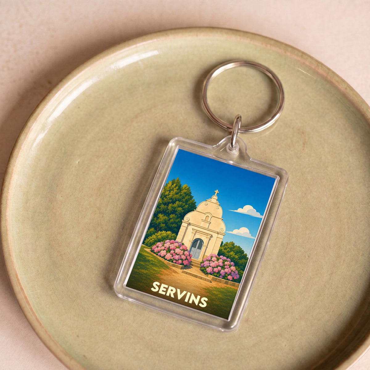 Porte-clés souvenir de la ville de Servins avec une illustration stylisée d'une chapelle entourée de fleurs.