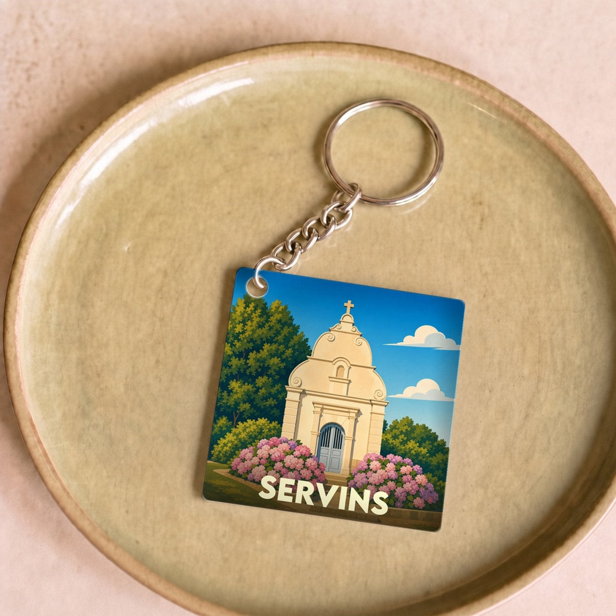 Porte-clés souvenir de la ville de Servins avec une illustration stylisée d'une chapelle entourée de fleurs.