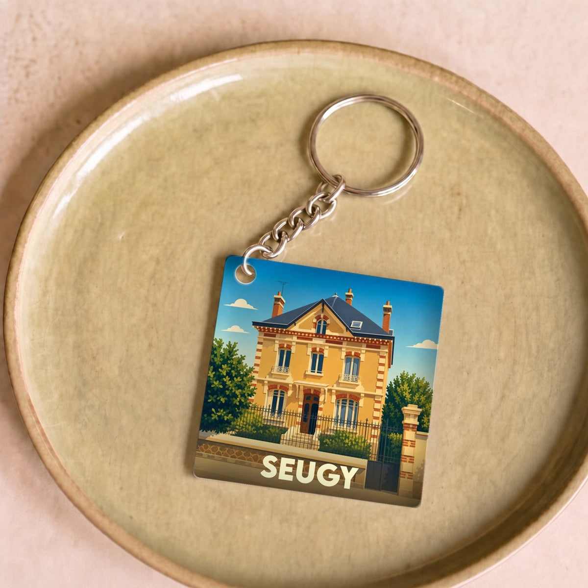 Porte-clés souvenir de la ville de Seugy avec une illustration stylisée d'une maison de maître.