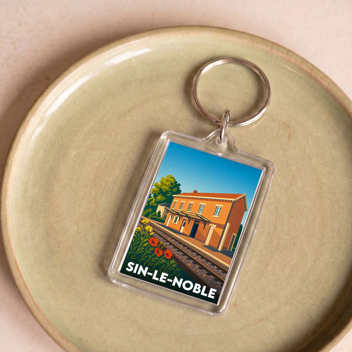 Porte-clés souvenir de la ville de Sin-le-Noble avec une illustration stylisée.