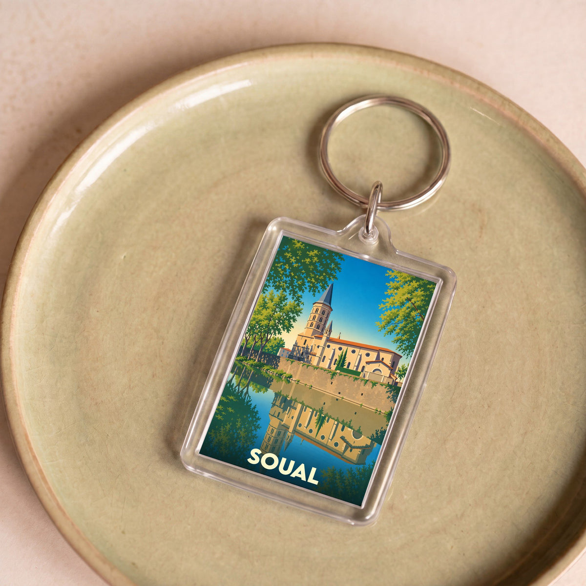 Porte-clés souvenir de la ville de Soual avec une illustration stylisée de son église se reflétant dans l'eau.