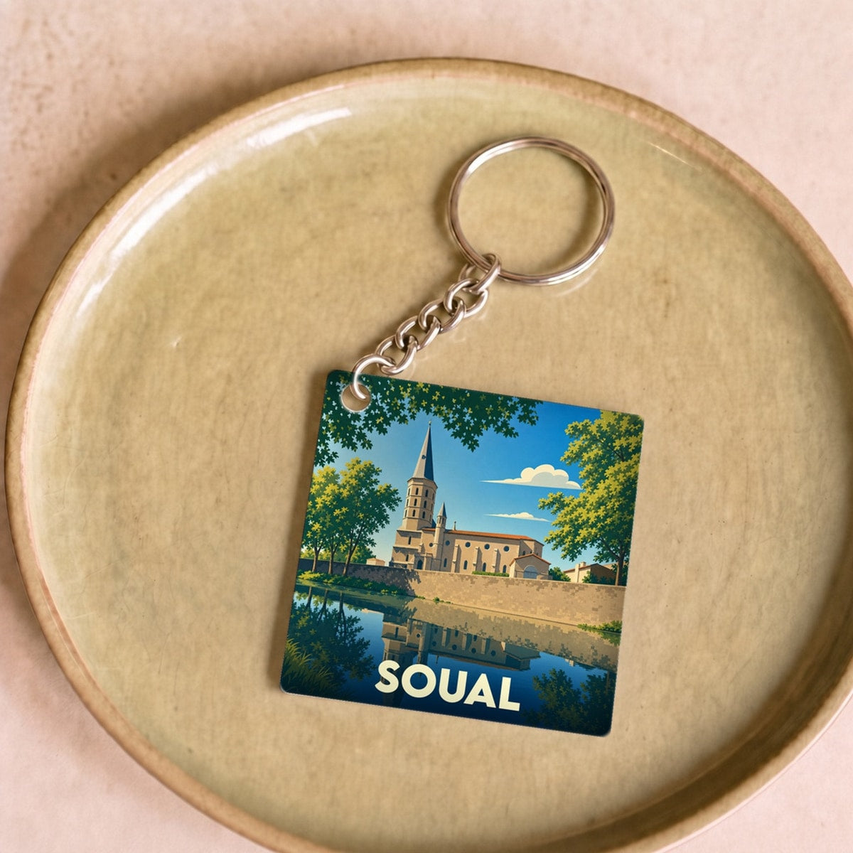 Porte-clés souvenir de la ville de Soual avec une illustration stylisée de son église se reflétant dans l'eau.