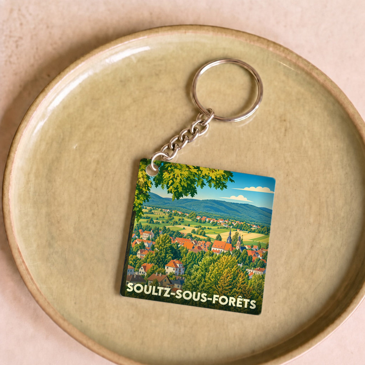 Porte-clés souvenir de la ville de Soultz-sous-Forêts avec une illustration paysagère stylisée.
