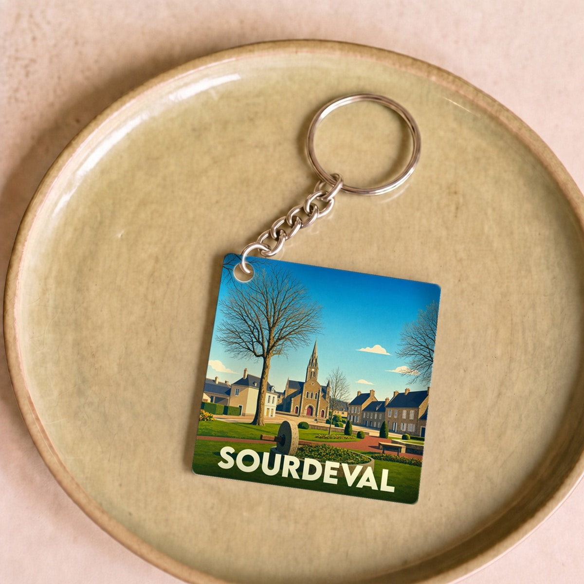 Porte-clés souvenir de la ville de Sourdeval avec une illustration stylisée.