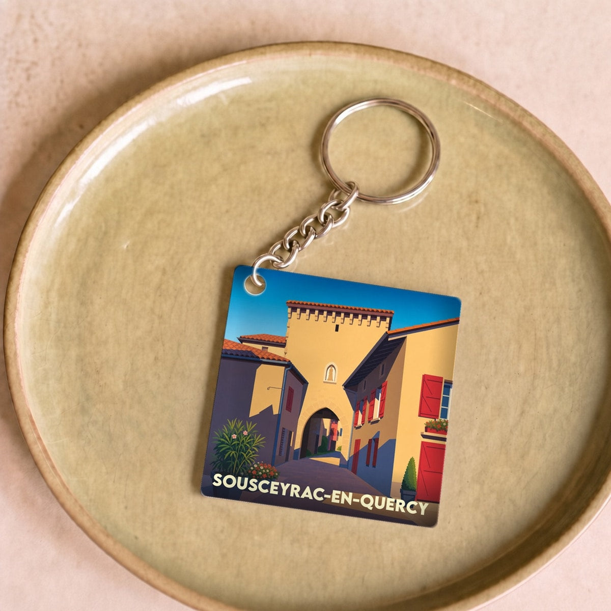 Porte-clés souvenir de la ville de Sousceyrac-en-Quercy avec une illustration stylisée.
