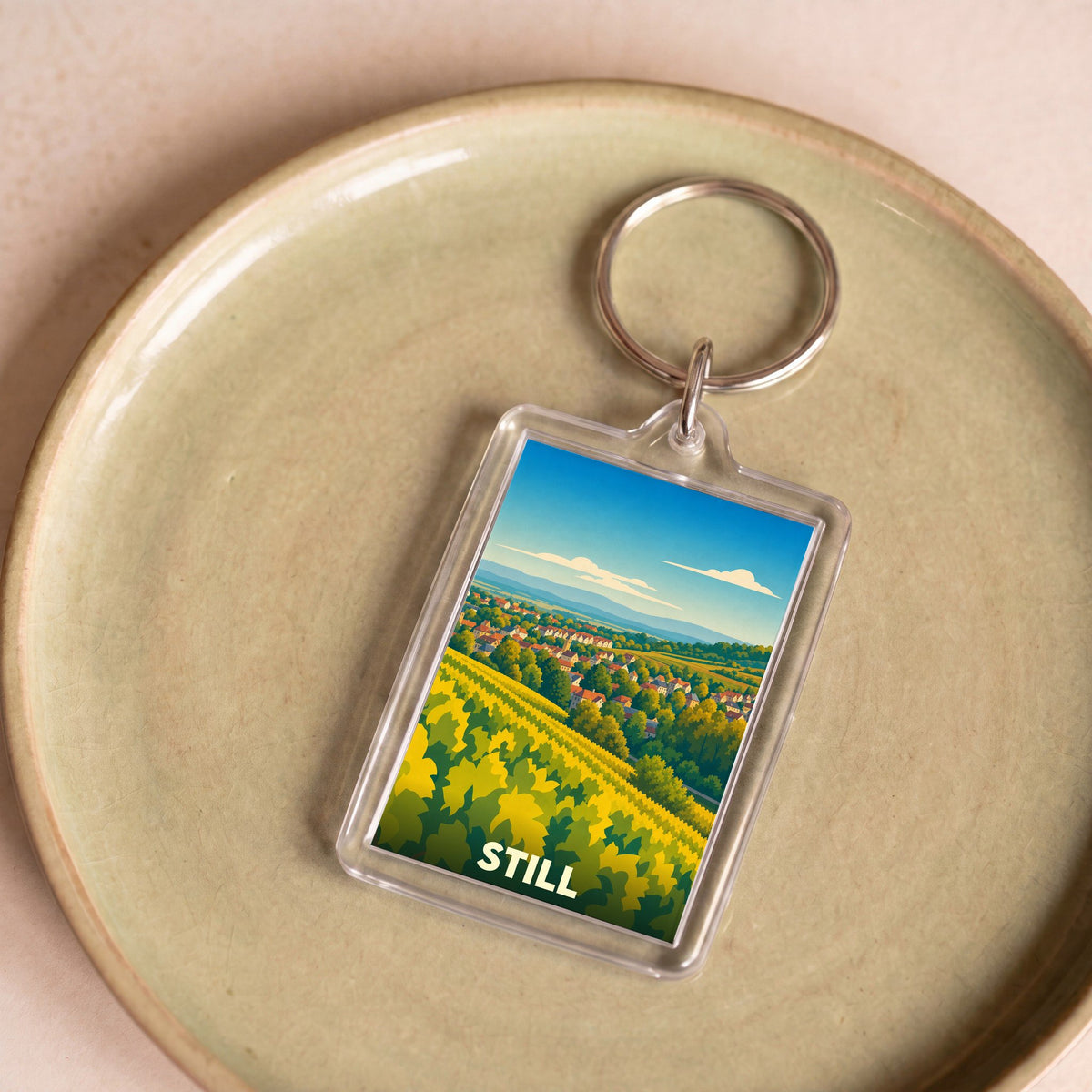 Porte-clés souvenir de la ville de Still avec une illustration stylisée d'un vignoble et d'un village.