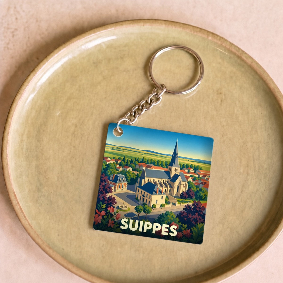 Porte-clés souvenir de la ville de Suippes avec une illustration stylisée d'une église et de paysages ruraux.