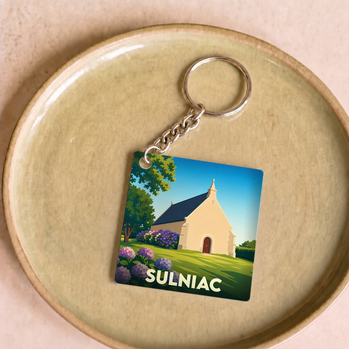 Porte-clés souvenir de la ville de Sulniac avec une illustration stylisée d'une chapelle entourée de fleurs.