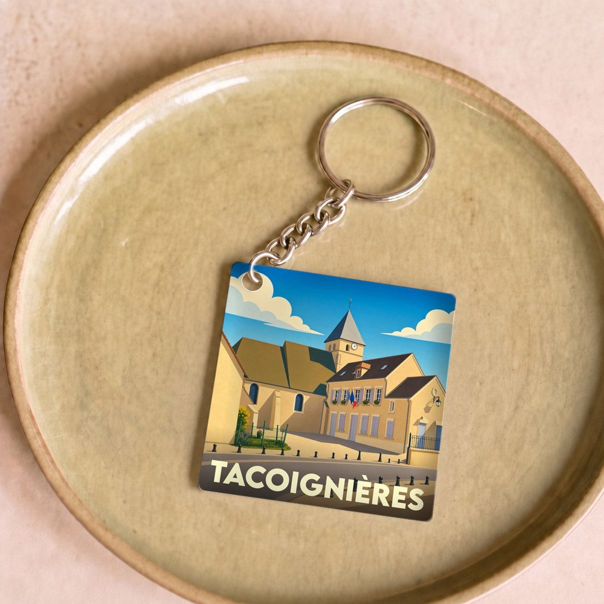 Porte-clés souvenir de la ville de Tacoignières avec une illustration stylisée.