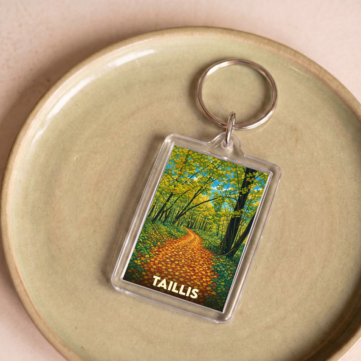 Porte-clés souvenir de la ville de Taillis avec une illustration stylisée d'un chemin forestier automnal.