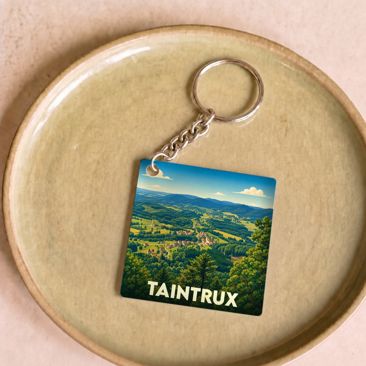 Porte-clés souvenir de la ville de Taintrux avec une illustration stylisée de son paysage vallonné.