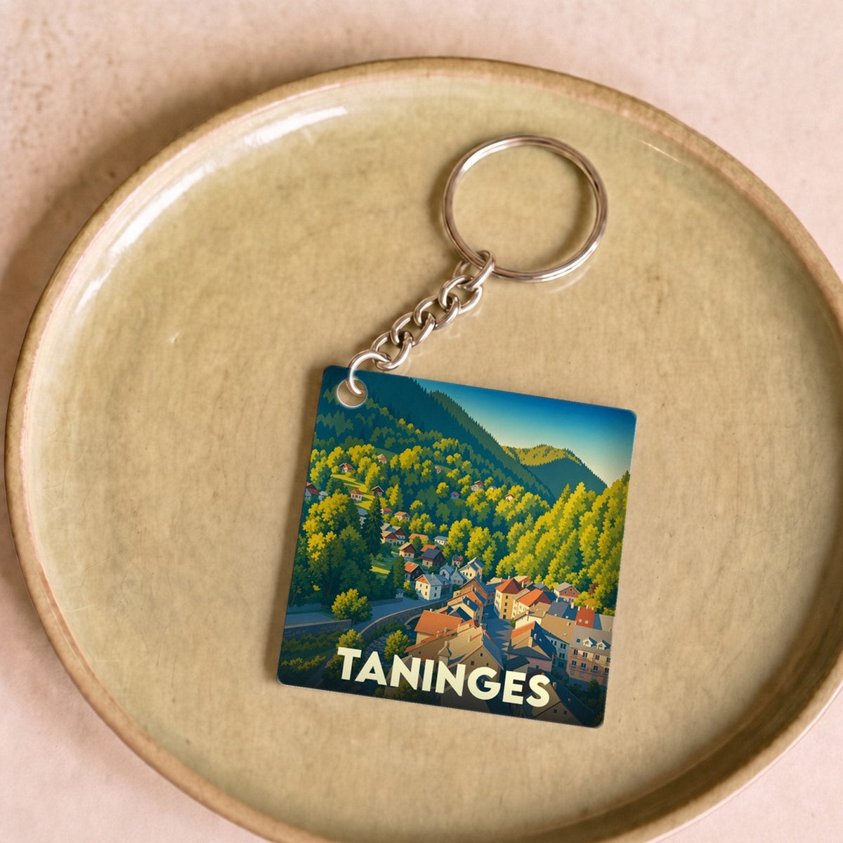 Porte-clés souvenir de la ville de Taninges avec une illustration stylisée de montagne.