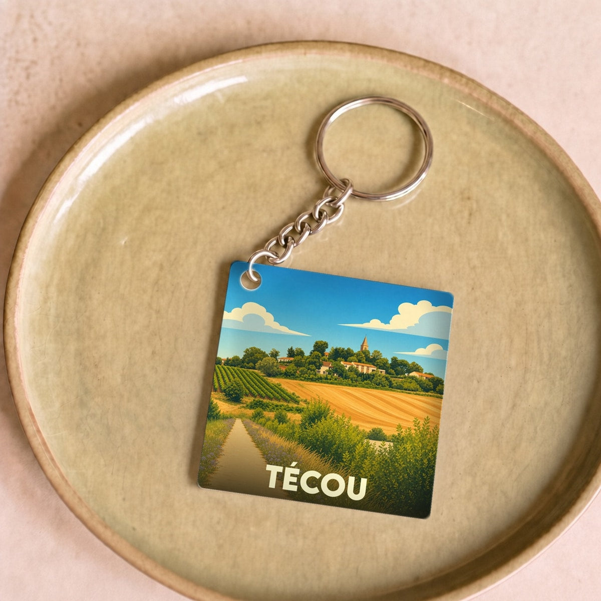 Porte-clés souvenir de la ville de Técou avec une illustration stylisée de son paysage rural.