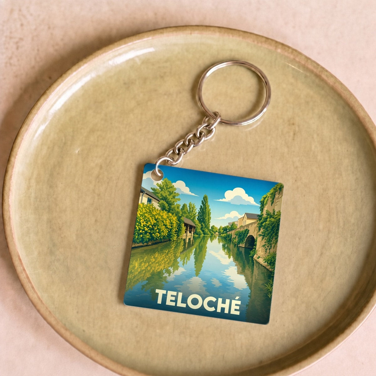 Porte-clés souvenir de la ville de Teloché avec une illustration stylisée d'un paysage de rivière.