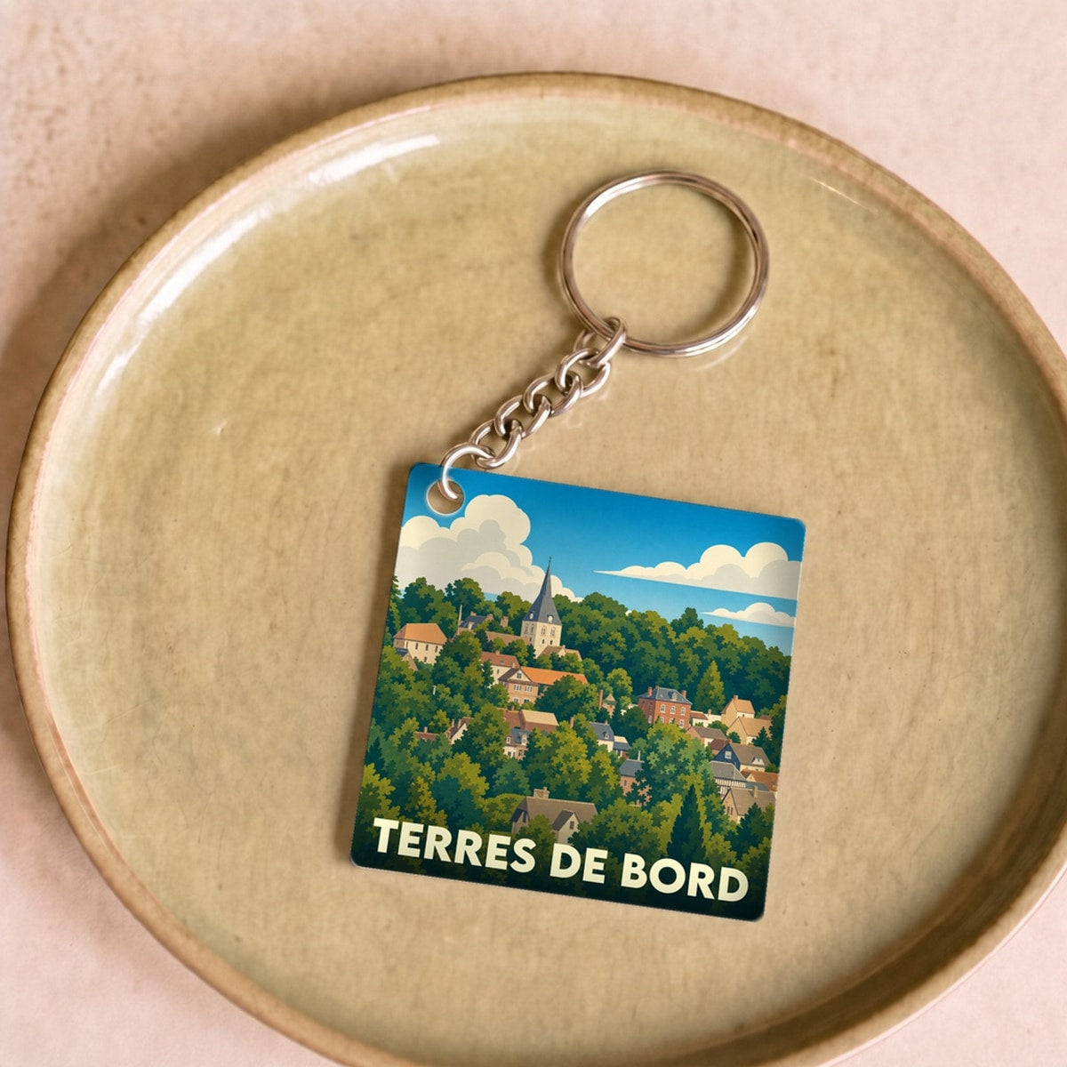 Porte-clés souvenir de Terres de Bord orné d'une illustration stylisée de la ville nichée dans la verdure.