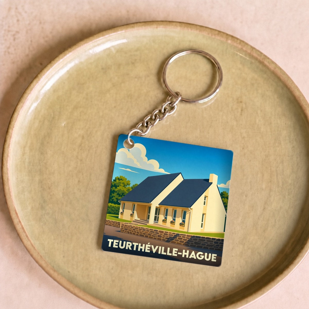 Porte-clés souvenir de la ville de Teurthéville-Hague avec une illustration stylisée d'une maison côtière.