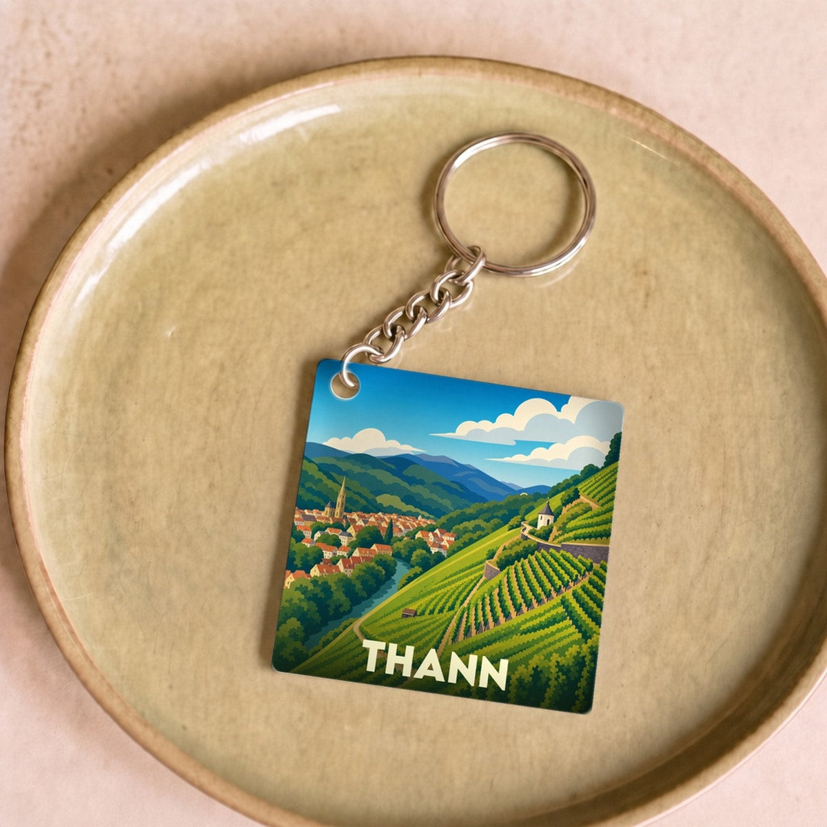 Porte-clés souvenir de la ville de Thann avec une illustration stylisée de ses vignobles et de son centre historique.