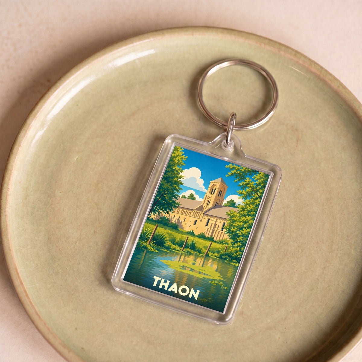 Porte-clés souvenir de la ville de Thaon avec une illustration stylisée de son église au bord de l'eau.