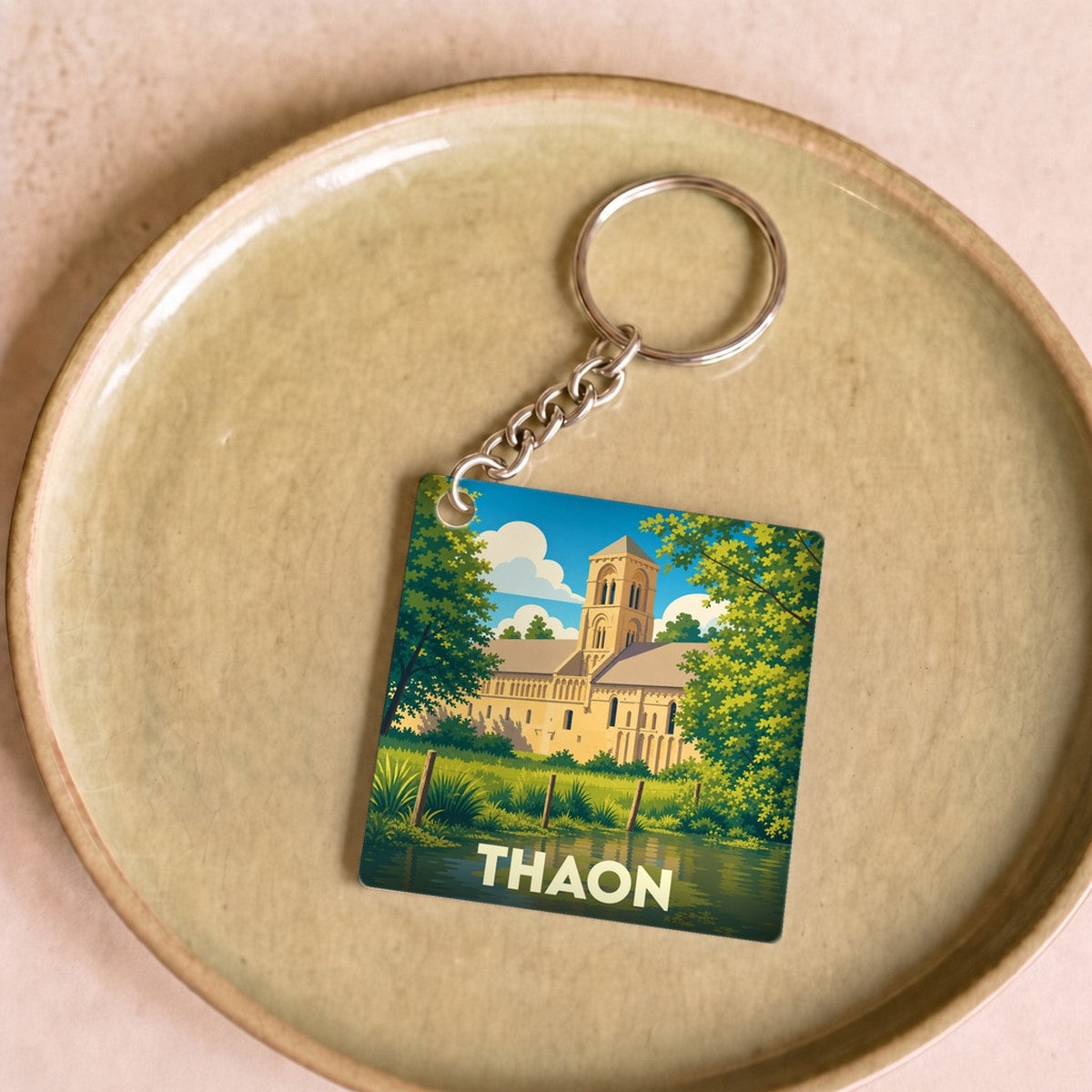Porte-clés souvenir de la ville de Thaon avec une illustration stylisée de son église au bord de l'eau.