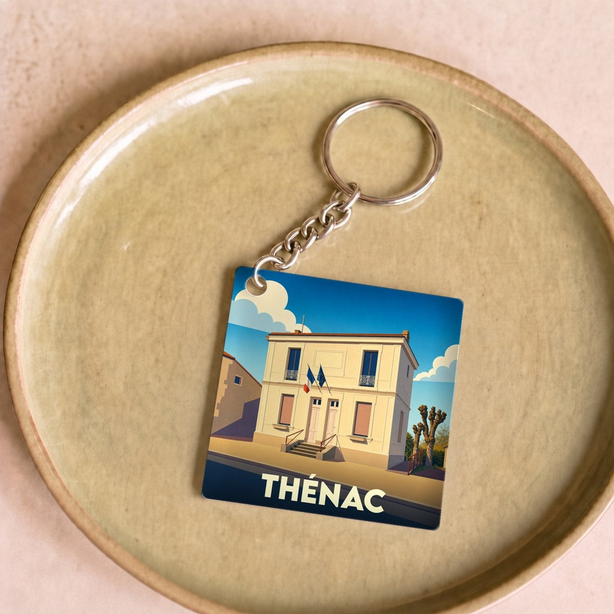 Porte-clés souvenir de la ville de Thénac avec une illustration stylisée de sa mairie.