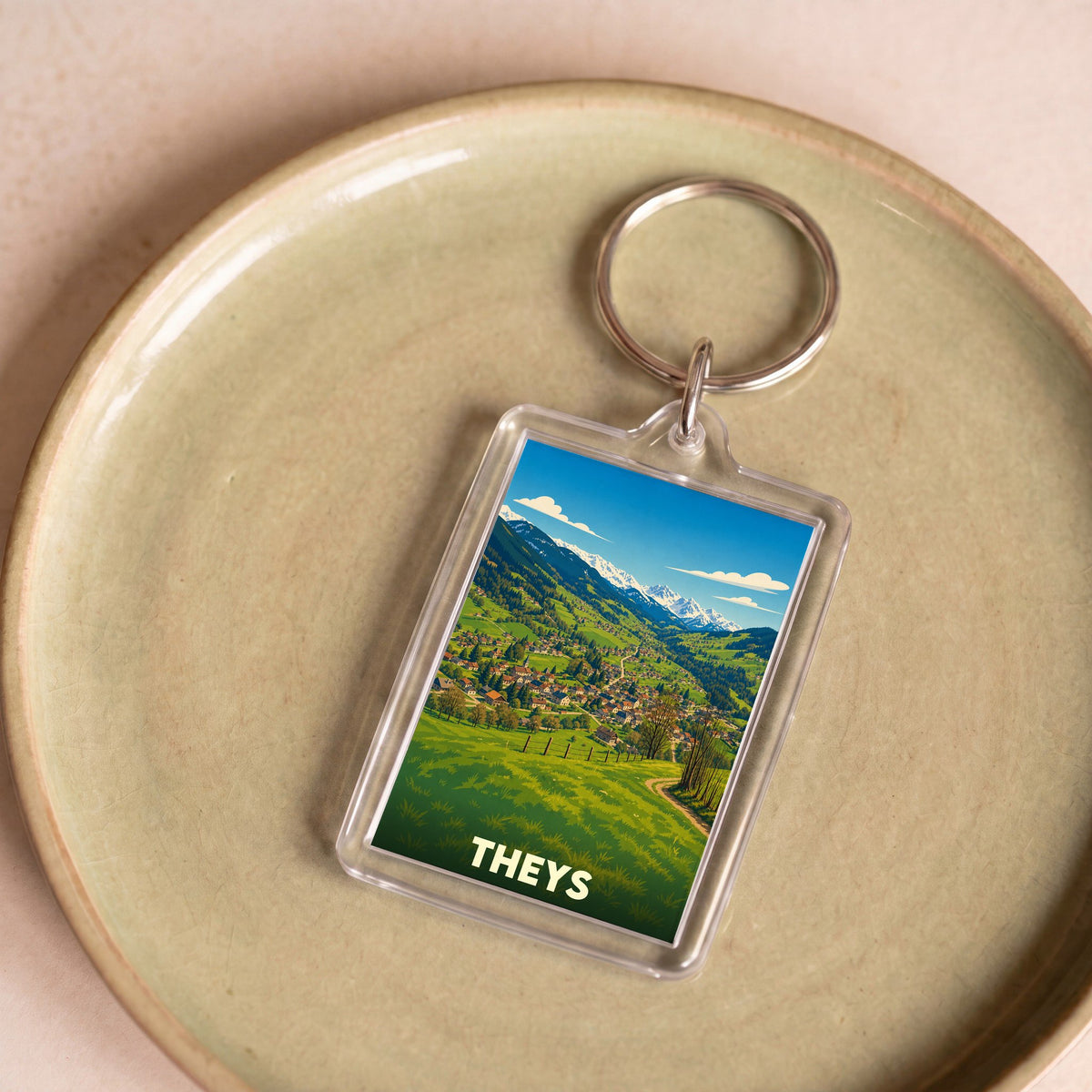 Porte-clés souvenir de la ville de Theys avec une illustration de paysage montagneux.