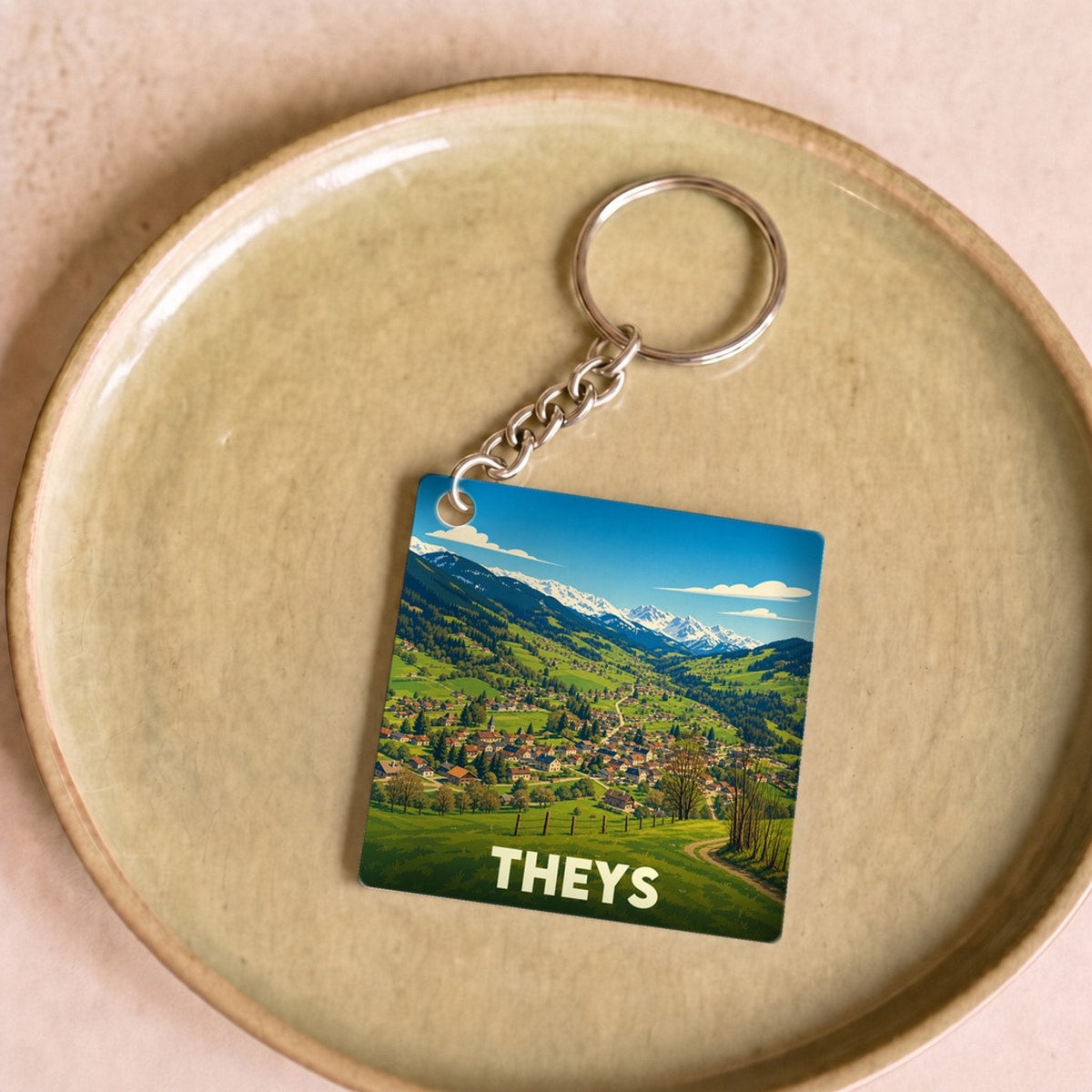 Porte-clés souvenir de la ville de Theys avec une illustration de paysage montagneux.