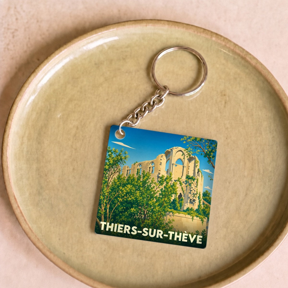 Porte-clés souvenir de la ville de Thiers-sur-Thève avec une illustration stylisée de ruines historiques.
