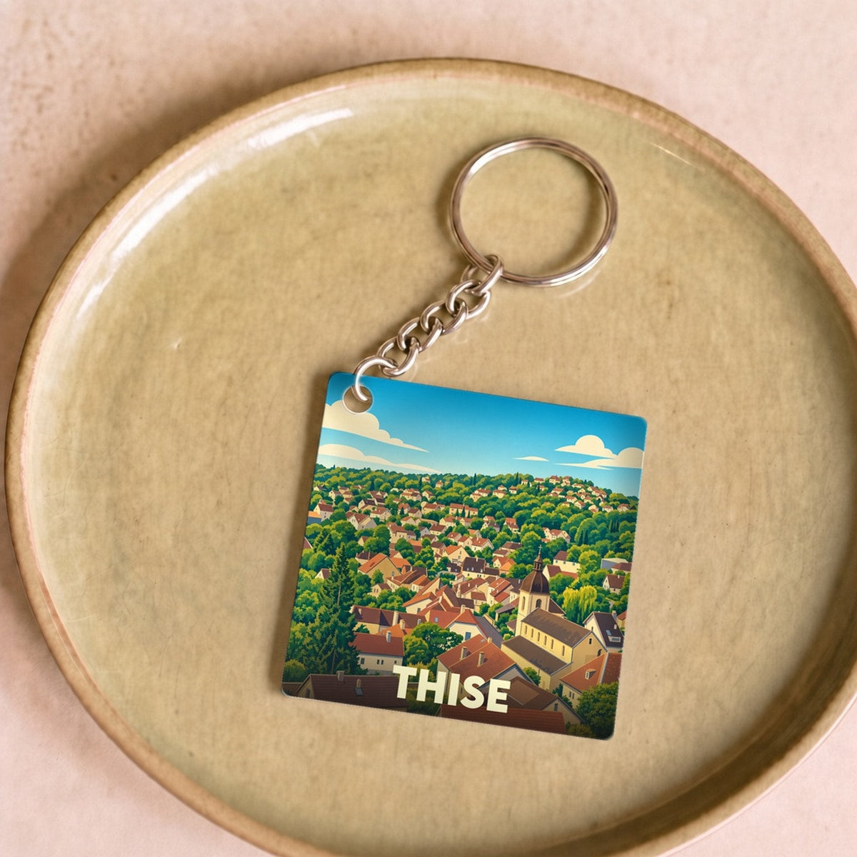 Porte-clés souvenir de la ville de Thise avec une illustration stylisée d'un paysage urbain verdoyant.