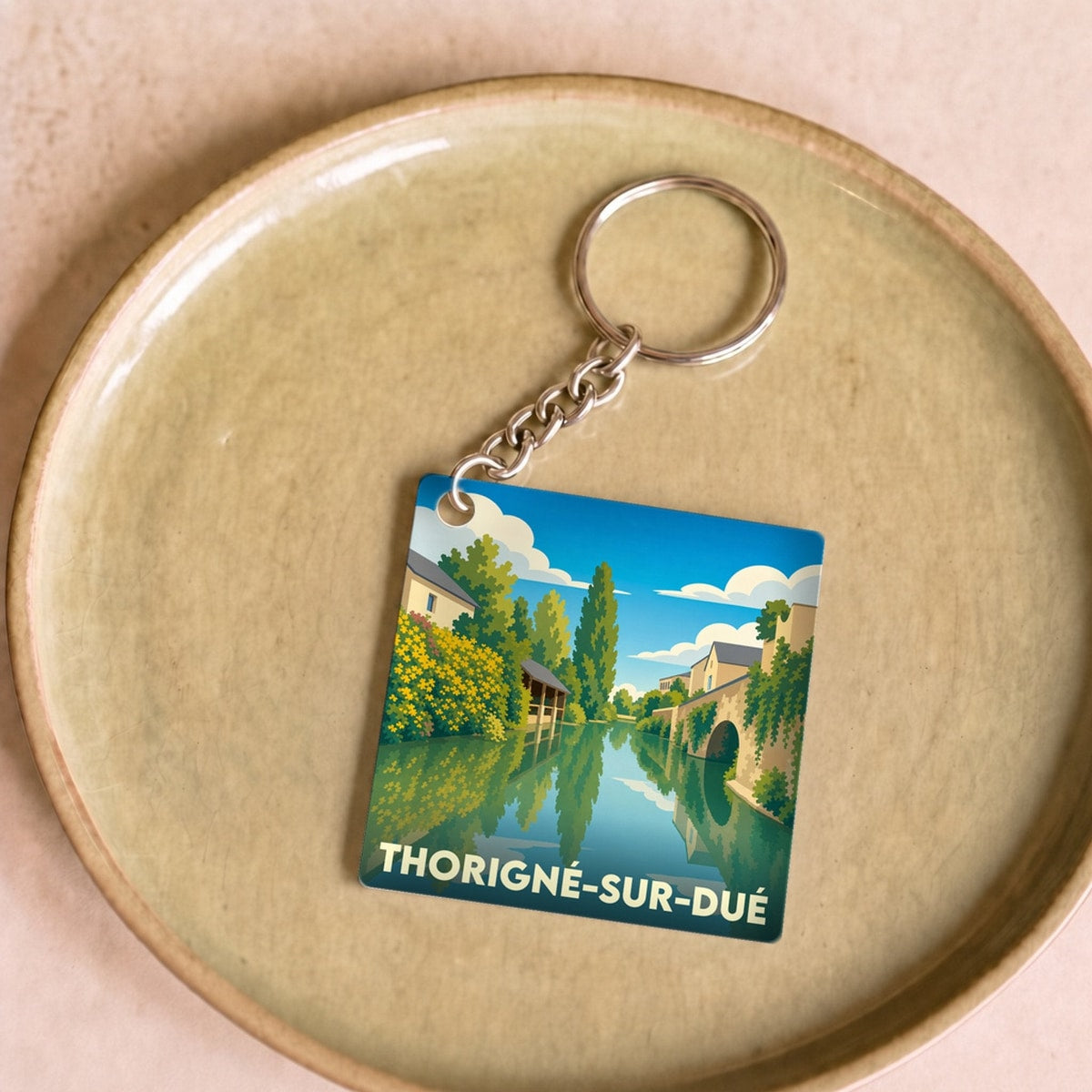 Porte-clés souvenir de la ville de Thorigné-sur-Dué avec une illustration stylisée d'un paysage fluvial.