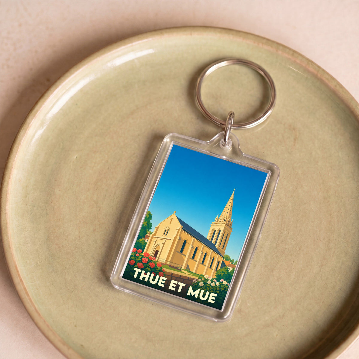 Porte-clés souvenir de la ville de Thue et Mue avec une illustration stylisée d'une église sous un ciel bleu.
