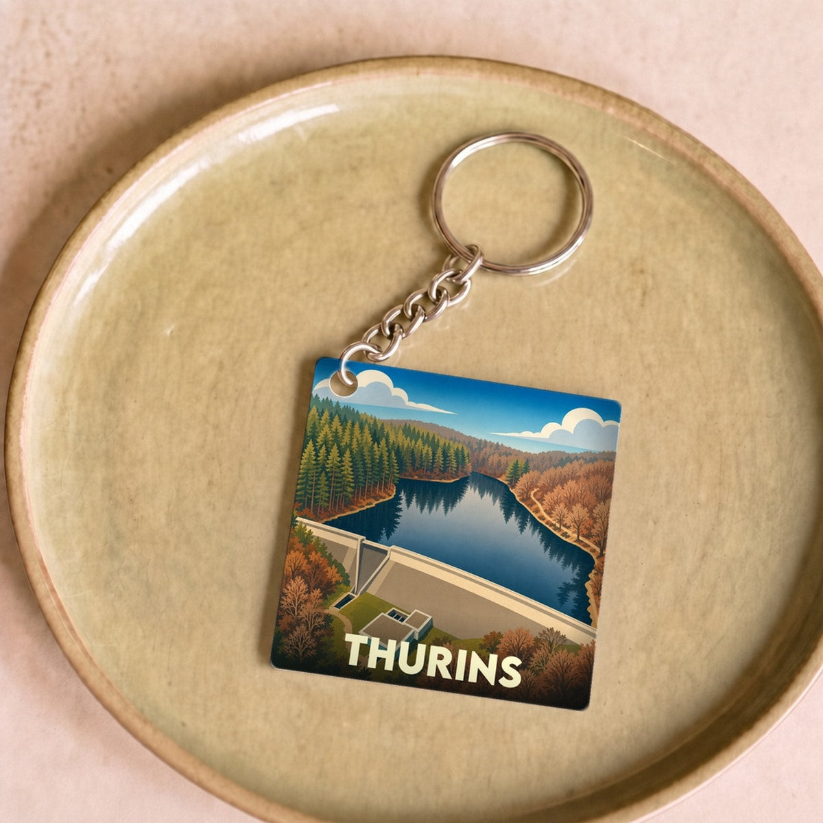 Porte-clés souvenir de la ville de Thurins avec une illustration stylisée d'un barrage et sa retenue d'eau.