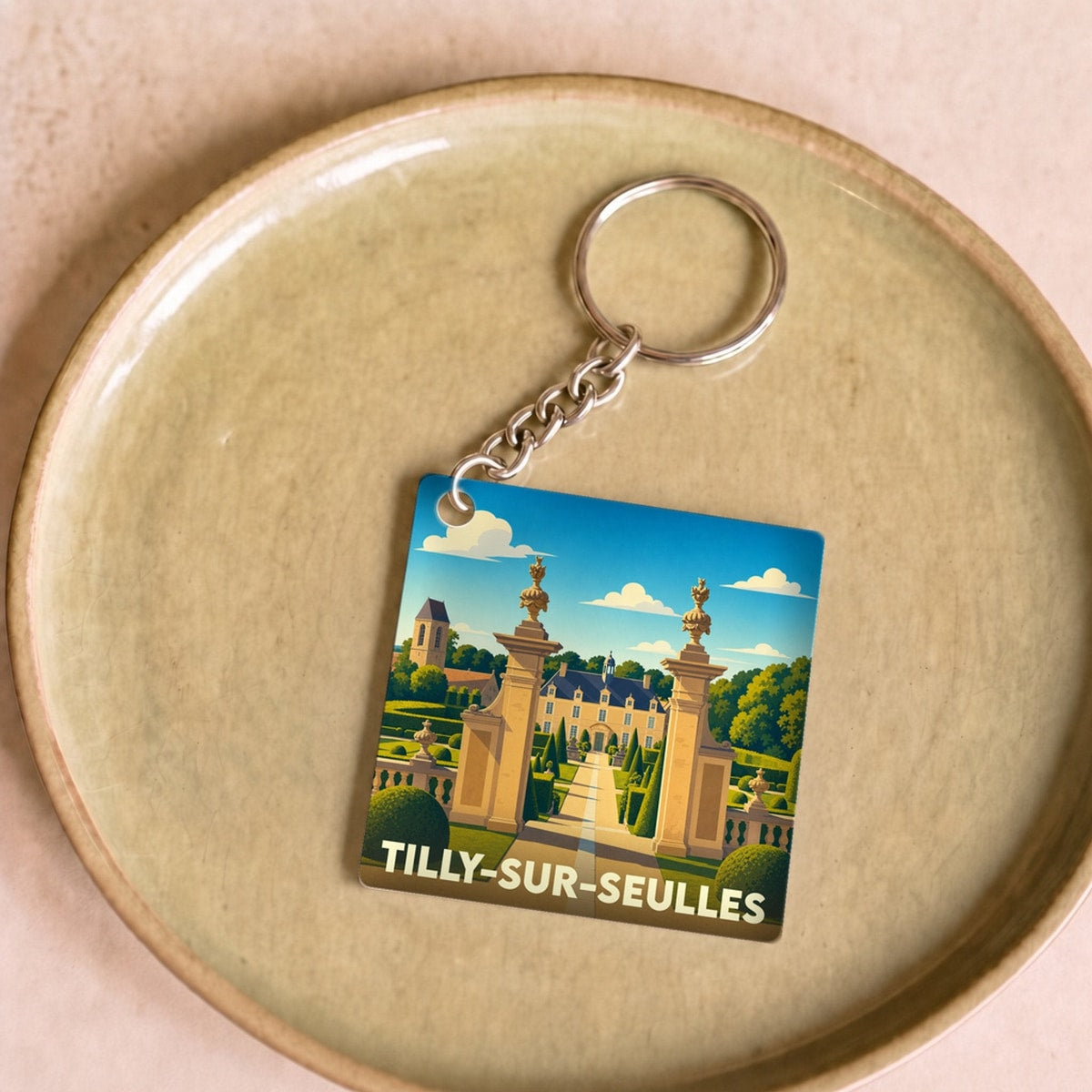 Porte-clés souvenir de la ville de Tilly-sur-Seulles avec une illustration stylisée d'un château et de son parc.