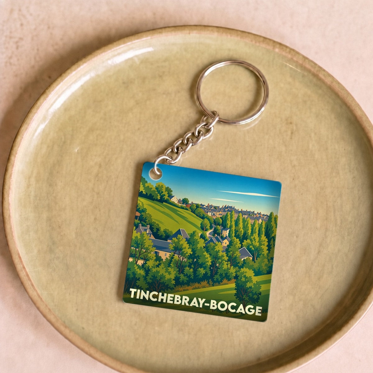 Porte-clés souvenir de la ville de Tinchebray-Bocage avec une illustration stylisée de son paysage verdoyant.