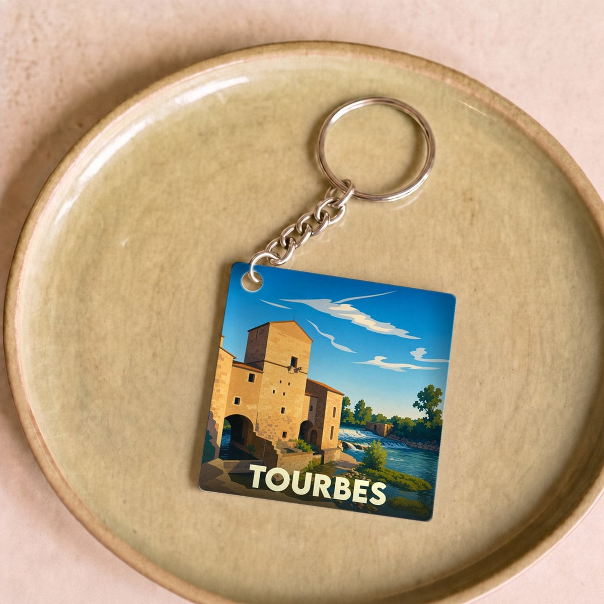 Porte-clés souvenir de la ville de Tourbes avec une illustration stylisée d'un bâtiment historique au bord de l'eau.