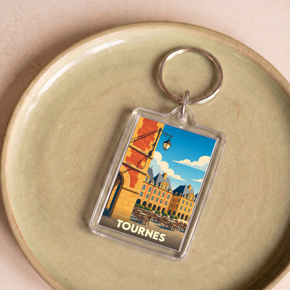 Porte-clés souvenir de la ville de Tournes avec une illustration stylisée de sa place centrale.